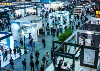 This photo captures the dynamic atmosphere of a trade show in full swing, showcasing an array of exhibitors and attendees. Under the bright lights of the venue, businesses and industry professionals gather to display their latest offerings, share insights, and create valuable connections. The strategic layout of the booths enhances visibility and facilitates interaction, making it an ideal environment for networking, learning, and fostering growth opportunities within the industry.