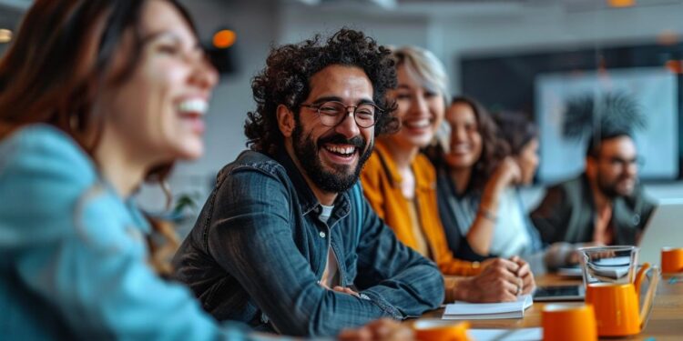 A group of diverse employees is captured in the midst of a light-hearted moment at work, displaying heartwarming smiles and infectious laughter. They appear to be sitting in a modern office setting, perhaps enjoying a break or engaging in a team-building activity. The atmosphere suggests a positive work culture where camaraderie and collaboration are encouraged, reinforcing the importance of a healthy work-life balance.