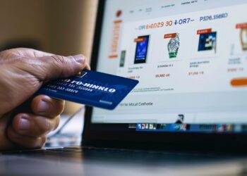 In this photo, we see a person's hand holding a credit card in front of a laptop displaying an online store's webpage. The image captures the moment of an e-commerce transaction, signifying the convenience and simplicity of purchasing goods and services in the digital age. This common scene highlights the blend of technology and commerce and how it has transformed the way consumers engage with retailers.