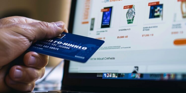 In this photo, we see a person's hand holding a credit card in front of a laptop displaying an online store's webpage. The image captures the moment of an e-commerce transaction, signifying the convenience and simplicity of purchasing goods and services in the digital age. This common scene highlights the blend of technology and commerce and how it has transformed the way consumers engage with retailers.